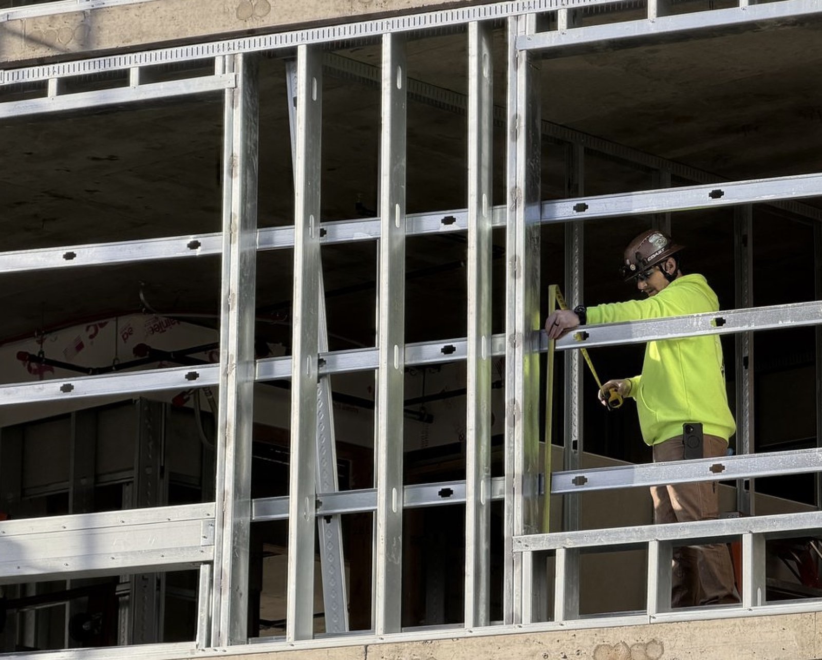 Beyond 9 crew member measuring a metal stud wall panel on an active commercial construction site